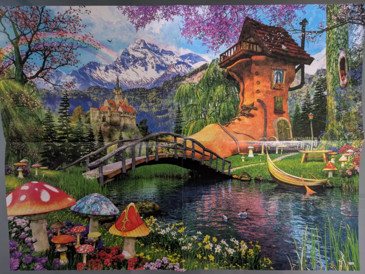 A whimsical landscape featuring a house shaped like a giant orange boot beside a stream with a bridge and snowy mountains.