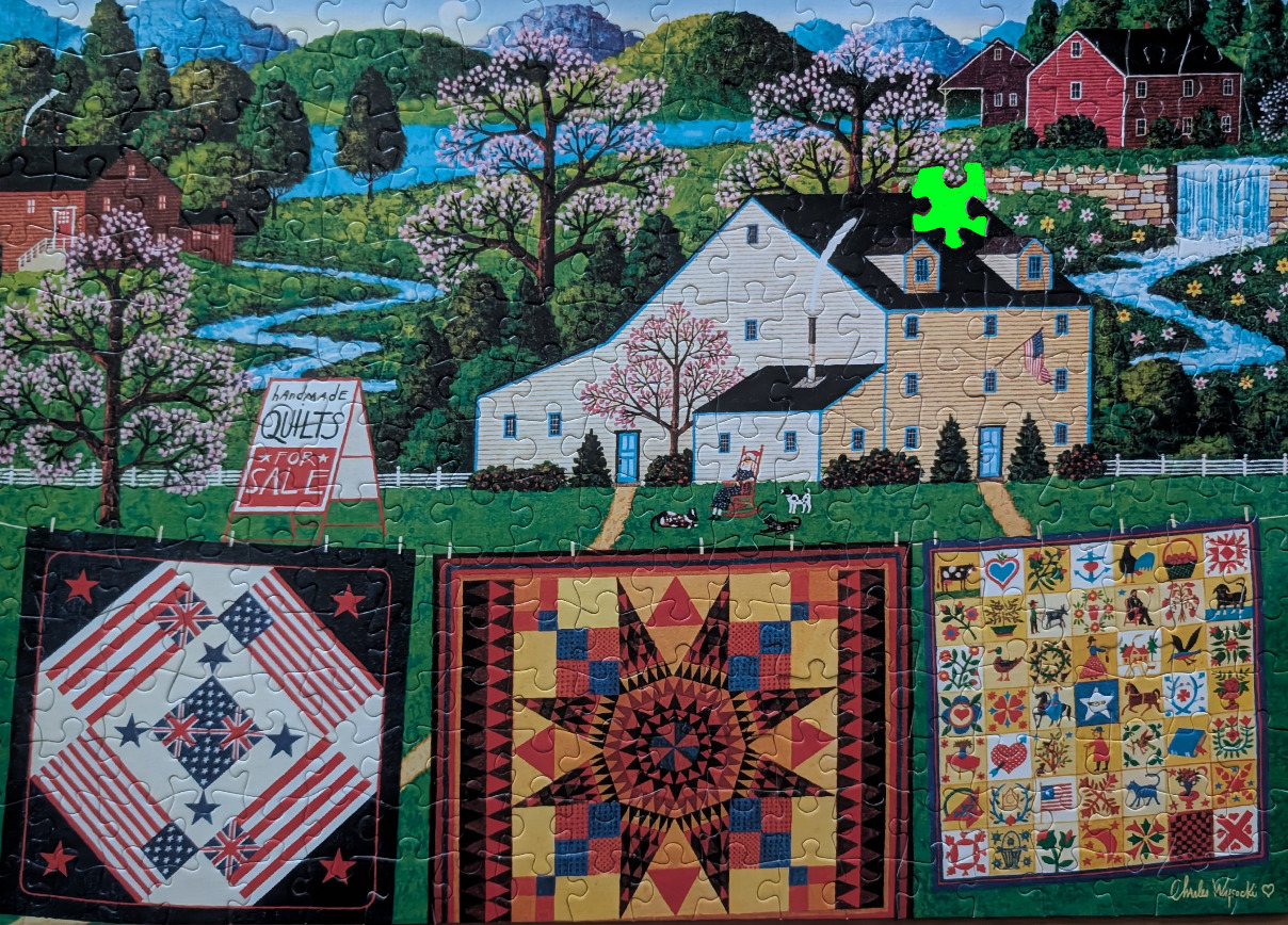 An idyllic folk art country scene featuring three hanging handmade quilts in the foreground and a large mill in the back.