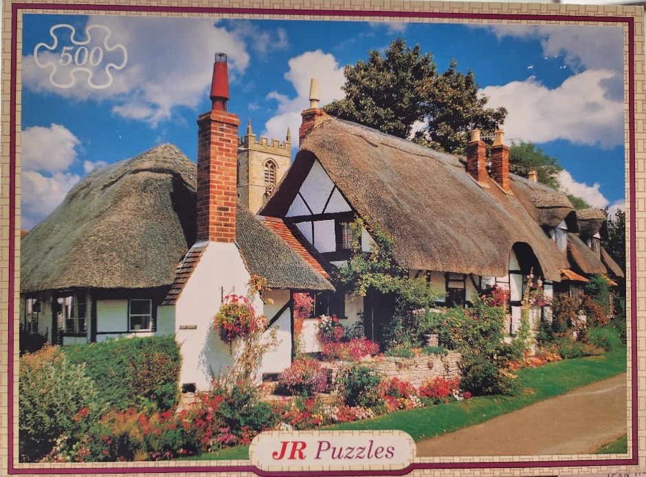 A row of traditional English thatched cottages with a church tower in the background under a blue sky.