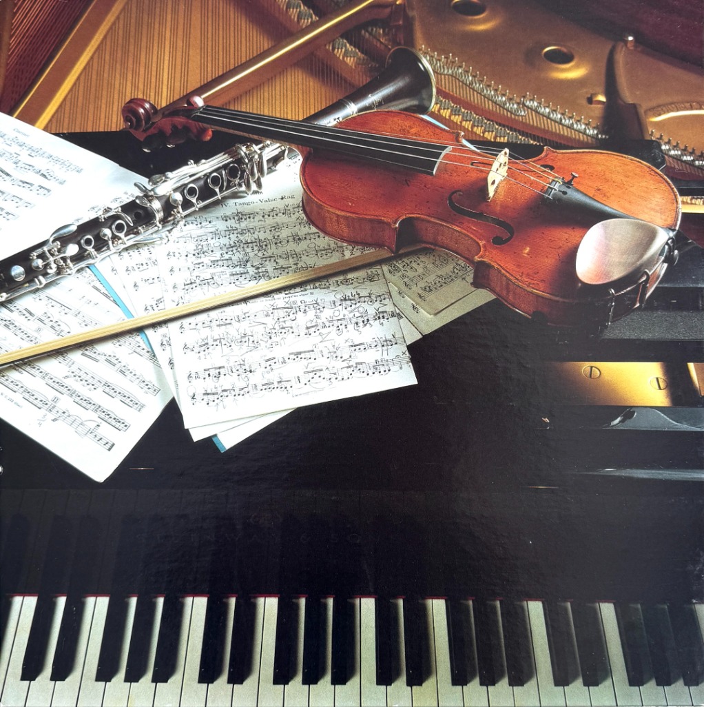 A violin, clarinet, and sheet music resting on a grand piano keyboard.