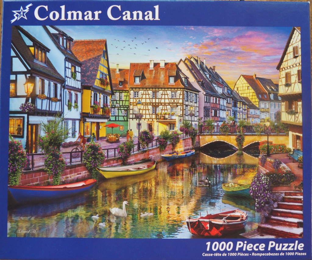A picturesque canal scene in Colmar with half-timbered houses, colorful boats, and a swan at sunset.