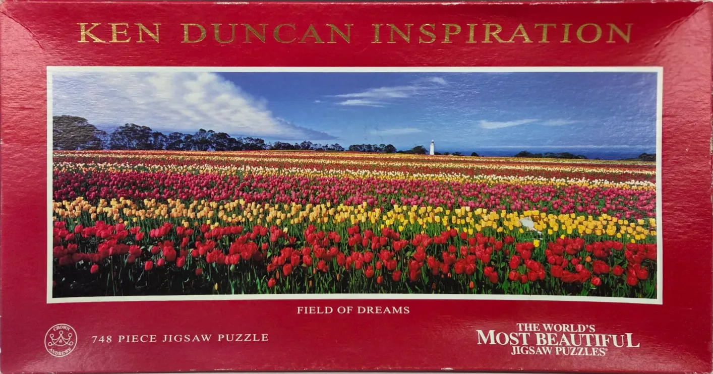A panoramic landscape photograph of a vast tulip field with a white lighthouse on the horizon.