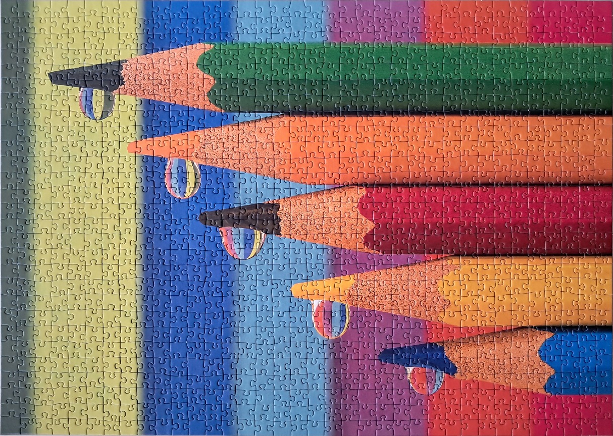 Five colored pencils arranged horizontally, each tipped with a realistic water droplet reflecting the background stripes.