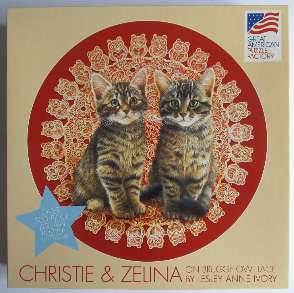 Two tabby kittens sitting on an ornate circular lace doily with an owl motif against a deep red background.
