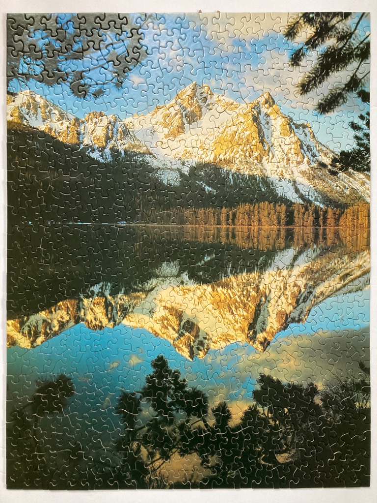 A stunning landscape photograph of the Sawtooth Mountains reflected in a calm, clear lake at sunrise.