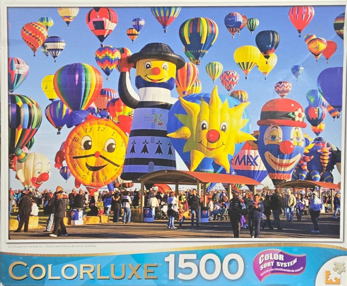 Many colorful and uniquely shaped hot air balloons floating in a clear blue sky over a crowd of people.