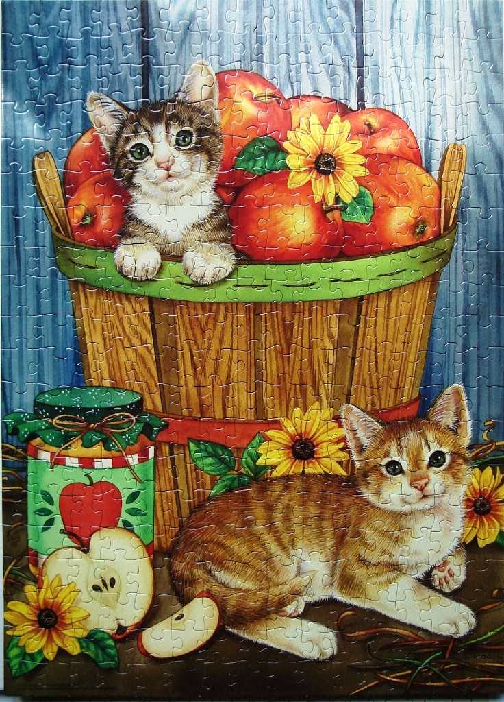 Two kittens with apples and sunflowers in a rustic wooden basket.