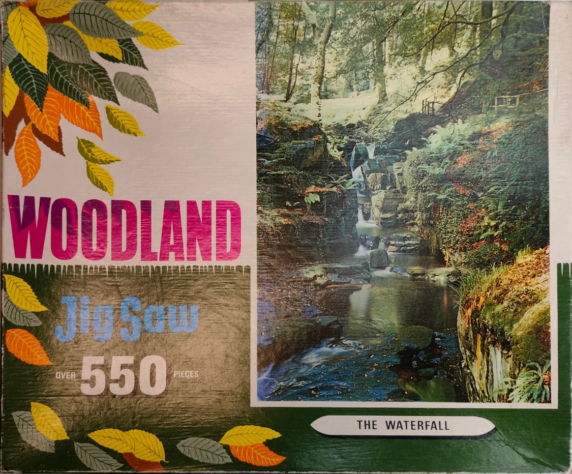 A photograph of a woodland stream cascading over rocky shelves in a deep, lush forest setting.