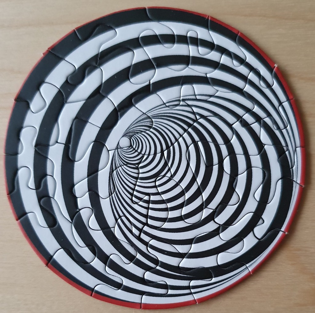 A circular optical illusion featuring a black and white hypnotic tunnel effect.