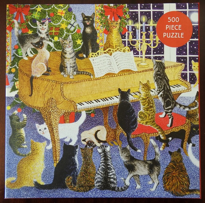 A group of many diverse cats gathered around and on top of a grand piano in a room decorated for Christmas.