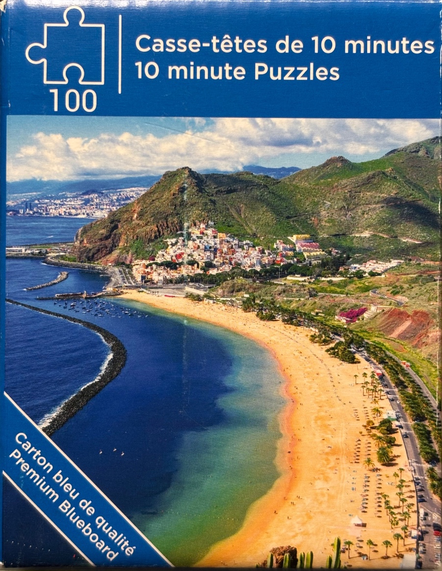 Aerial view of Teresitas Beach in Tenerife with a coastal town at the base of green mountains.