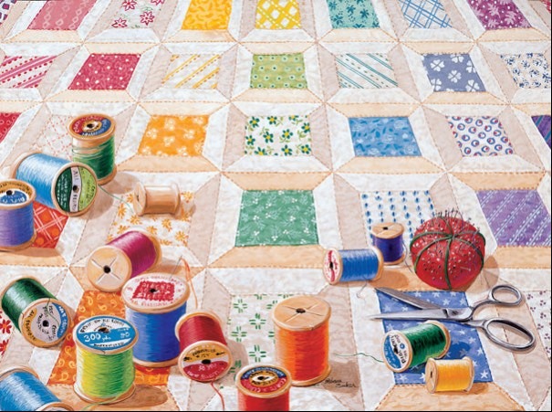 A collection of colorful sewing thread spools, scissors, and a pincushion resting on a patchwork quilt.
