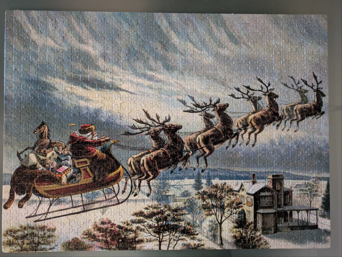Santa Claus in his sleigh pulled by reindeer flying over a snow-covered house at twilight