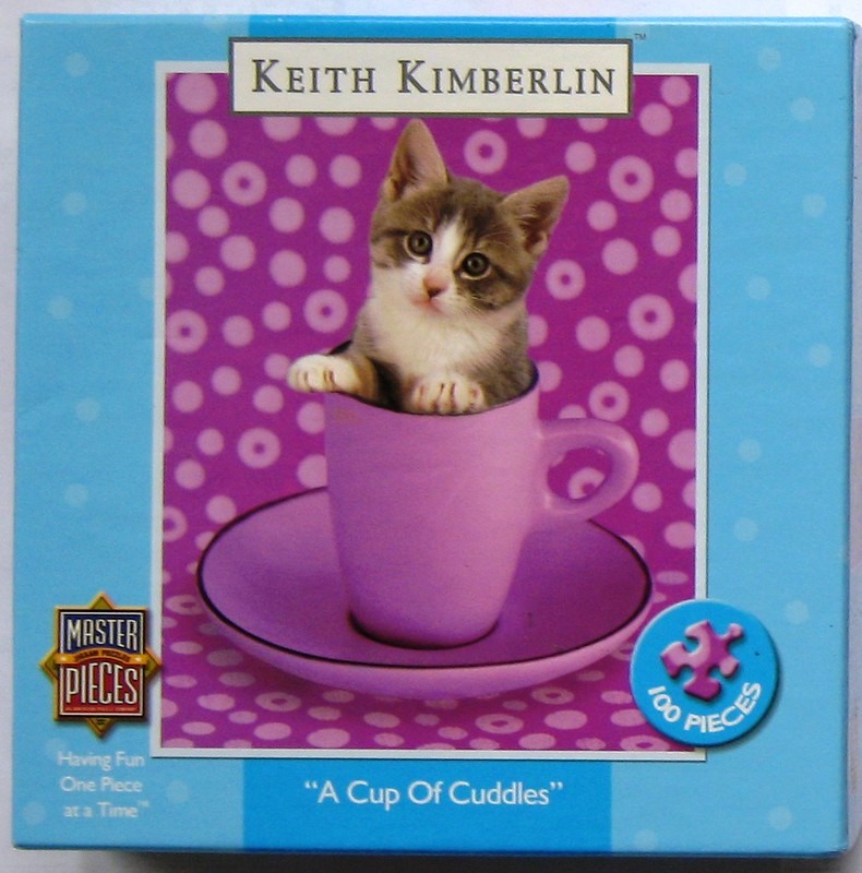 A cute tabby and white kitten sitting inside a purple teacup against a polka-dot background.