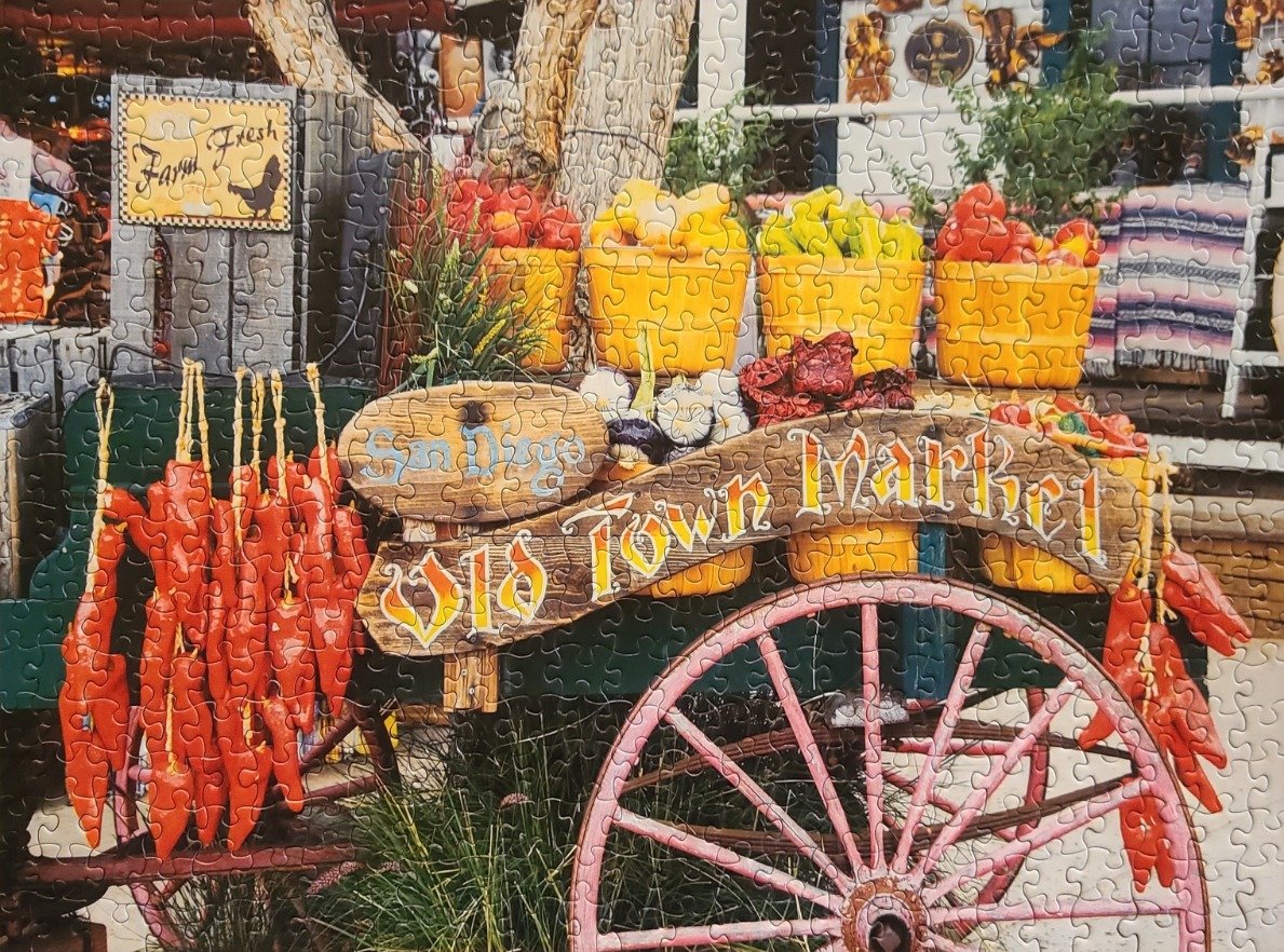 A rustic wooden wagon at the Old Town Market in San Diego, decorated with baskets of produce and hanging red chili ristras.