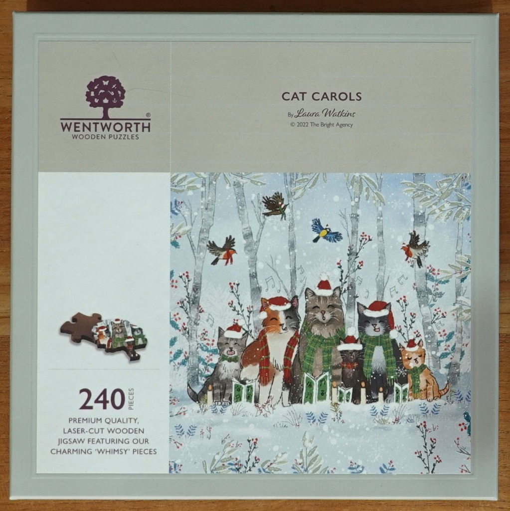 An illustration of six cats wearing Santa hats and scarves, singing carols in a snowy, birch-filled forest.
