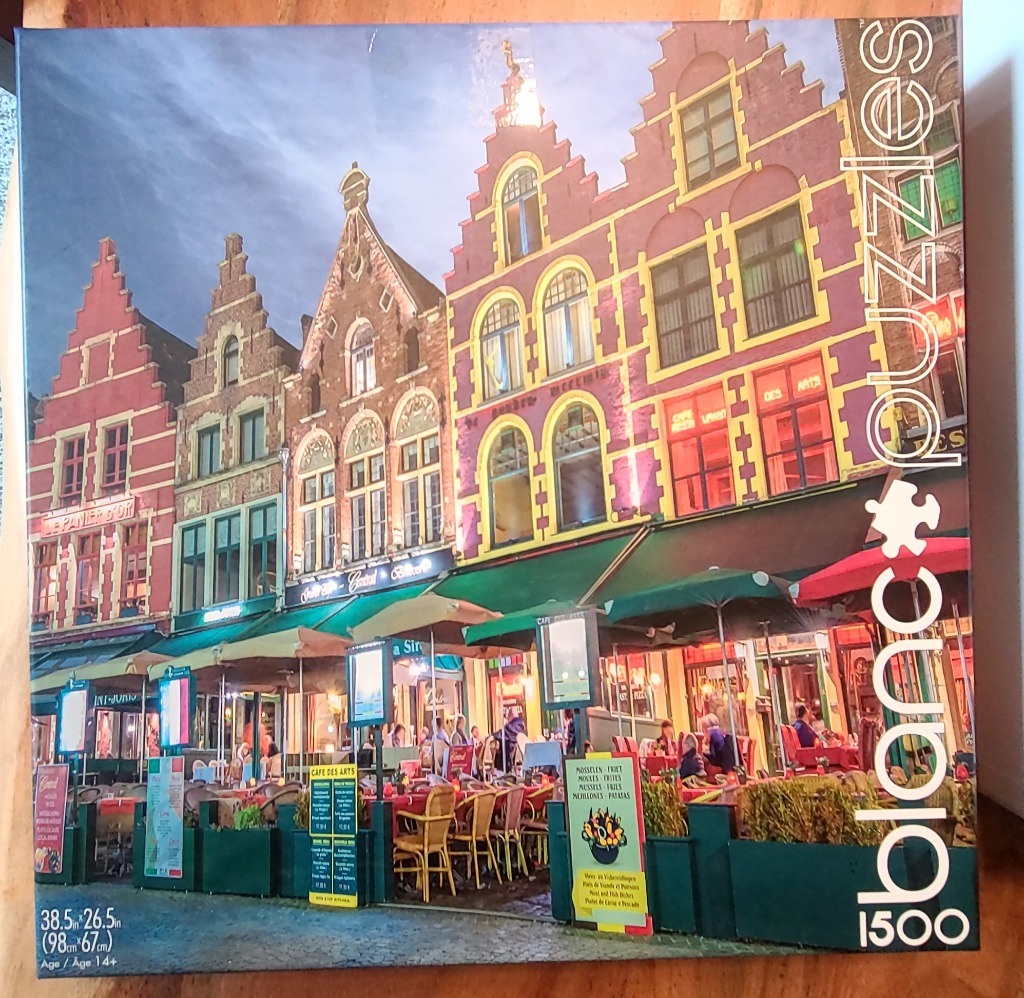 A row of historic buildings with stepped gables over outdoor restaurant terraces at dusk.