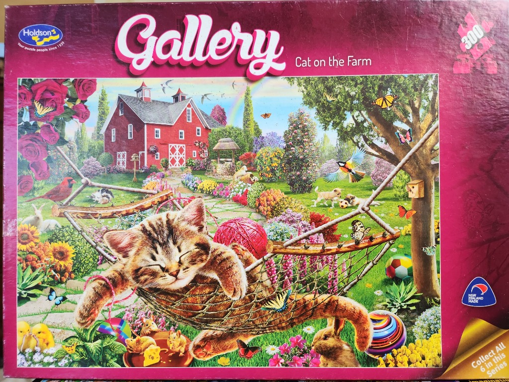 A tabby kitten sleeping in a hammock in a vibrant country garden with a red barn in the background.
