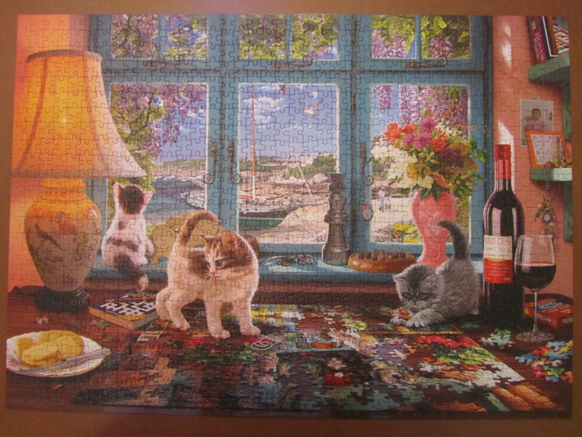 Three kittens on a table with a view of a harbor through a window, near a lamp, flowers, and a bottle of wine.