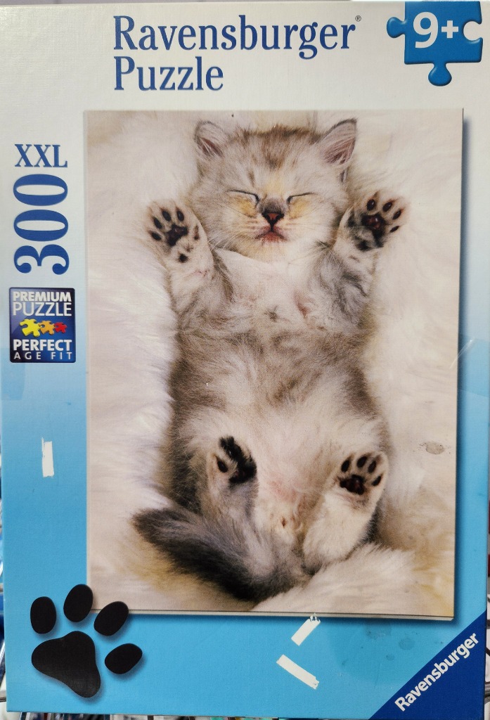 A fluffy gray and white kitten sleeping on its back on a soft white surface.