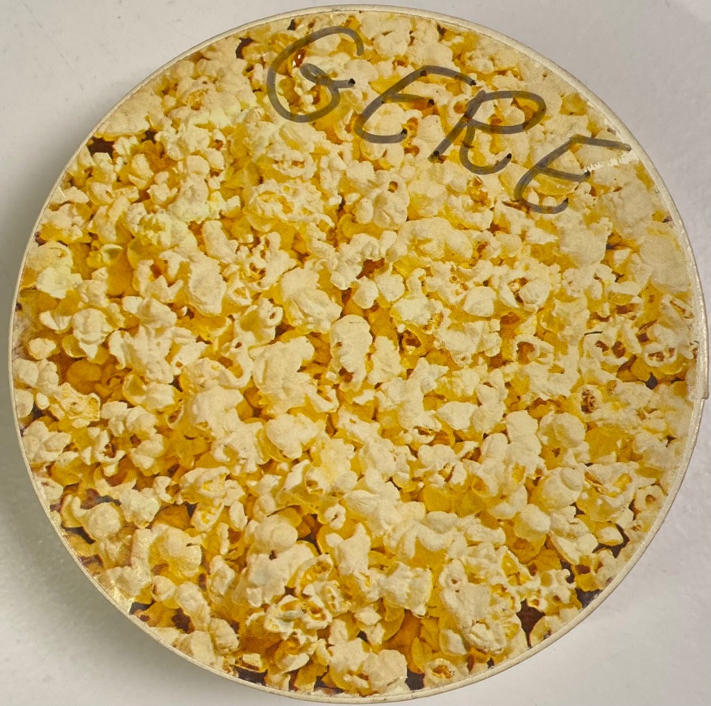 Circular image of a pile of buttery popcorn with the handwritten word GERE across the top