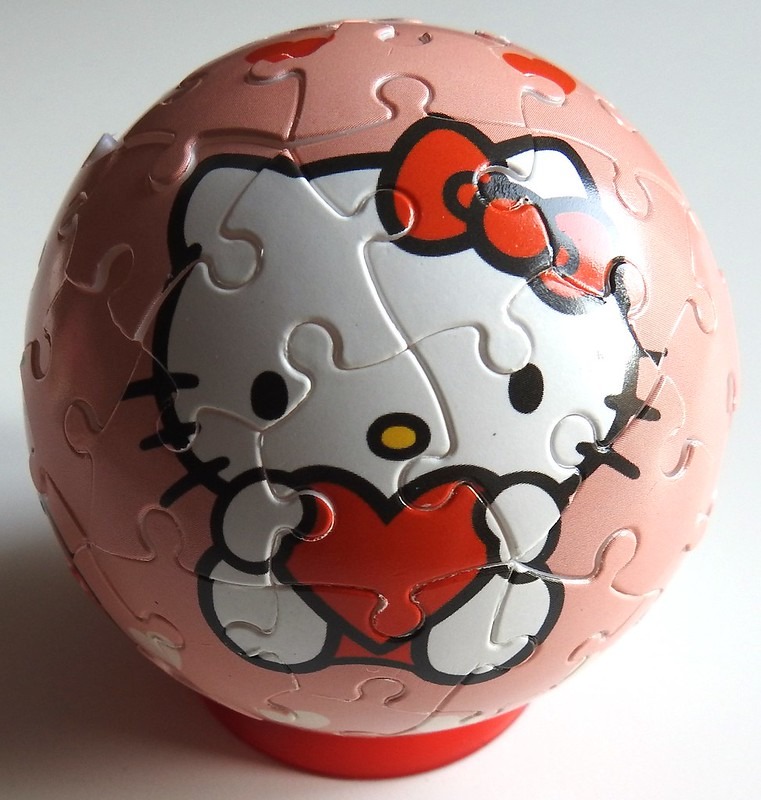 A spherical object featuring an illustration of Hello Kitty holding a red heart on a pastel pink background.