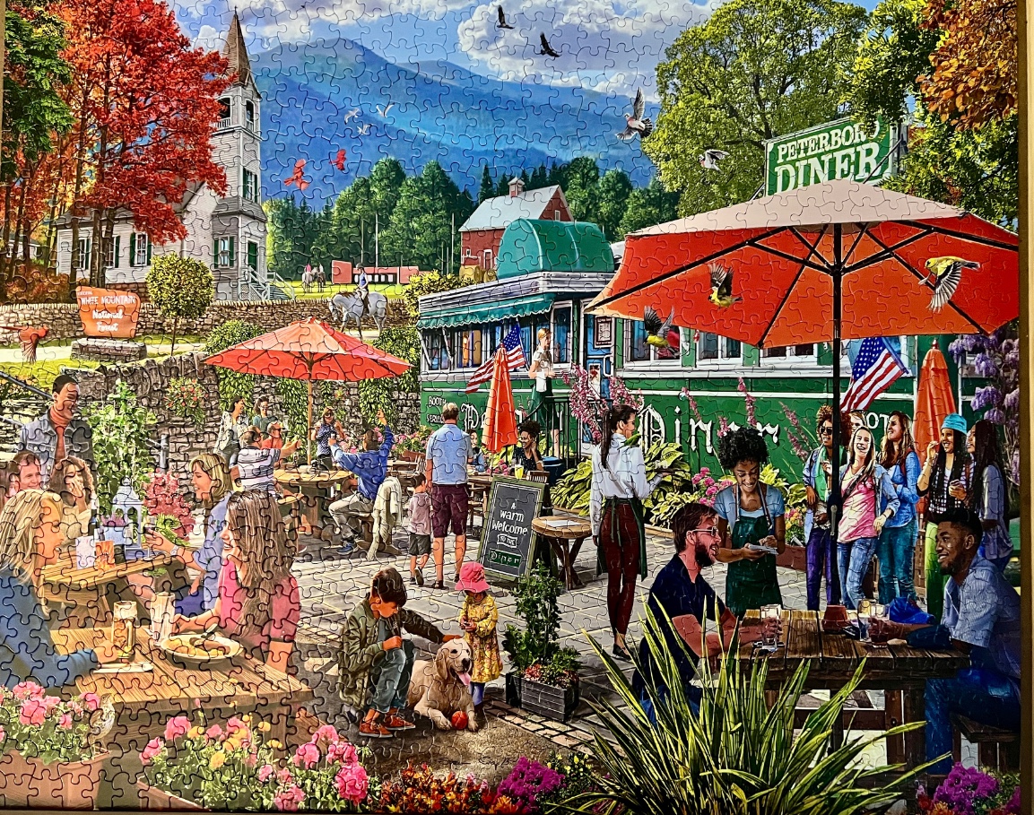 Outdoor scene of a busy diner patio in autumn with a church and mountains in the background.