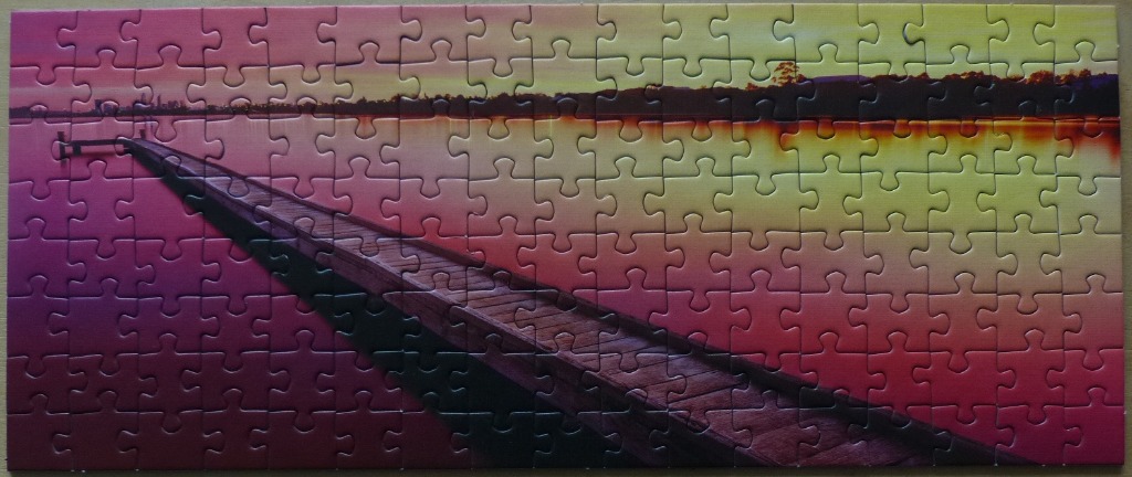 Panoramic view of a wooden pier stretching into a tranquil lake at sunset with pink and yellow sky