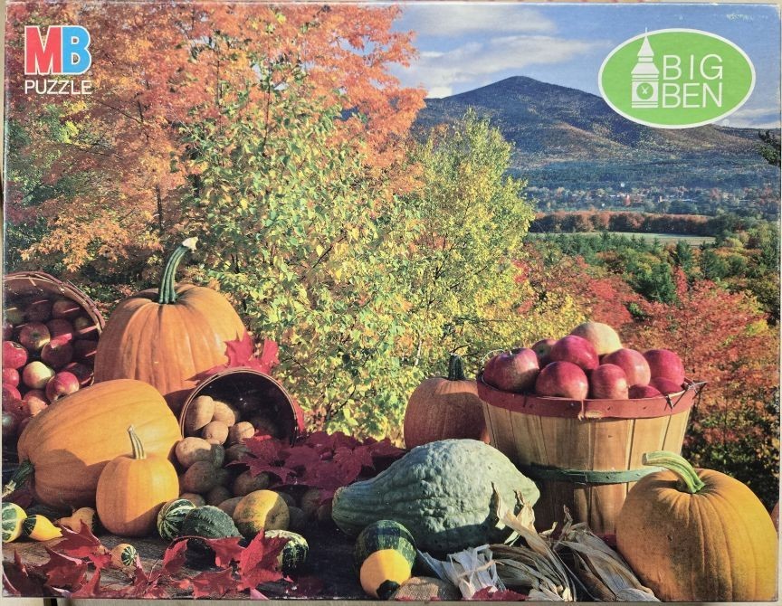 Autumn harvest scene with pumpkins, apples, and a mountain landscape background.