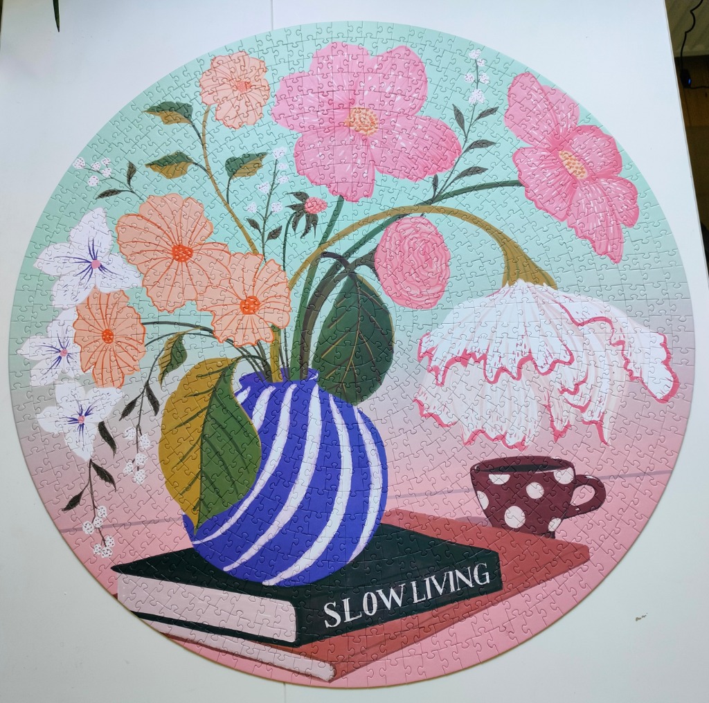 An illustration of a blue-striped vase filled with flowers sitting on a book titled SLOW LIVING next to a polka-dot cup.
