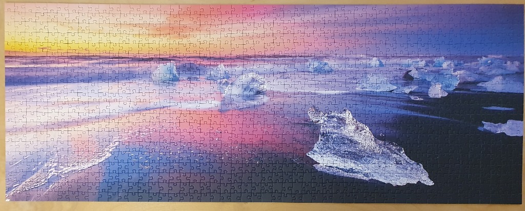 Panoramic view of icy blue icebergs on a black sand beach during a vibrant pink and orange sunset.