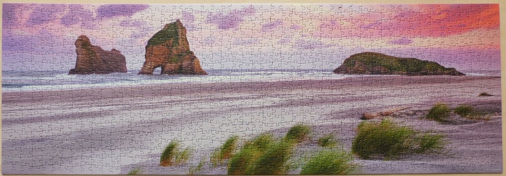Panoramic view of Wharariki Beach in New Zealand at sunset with sea stacks and grassy dunes.