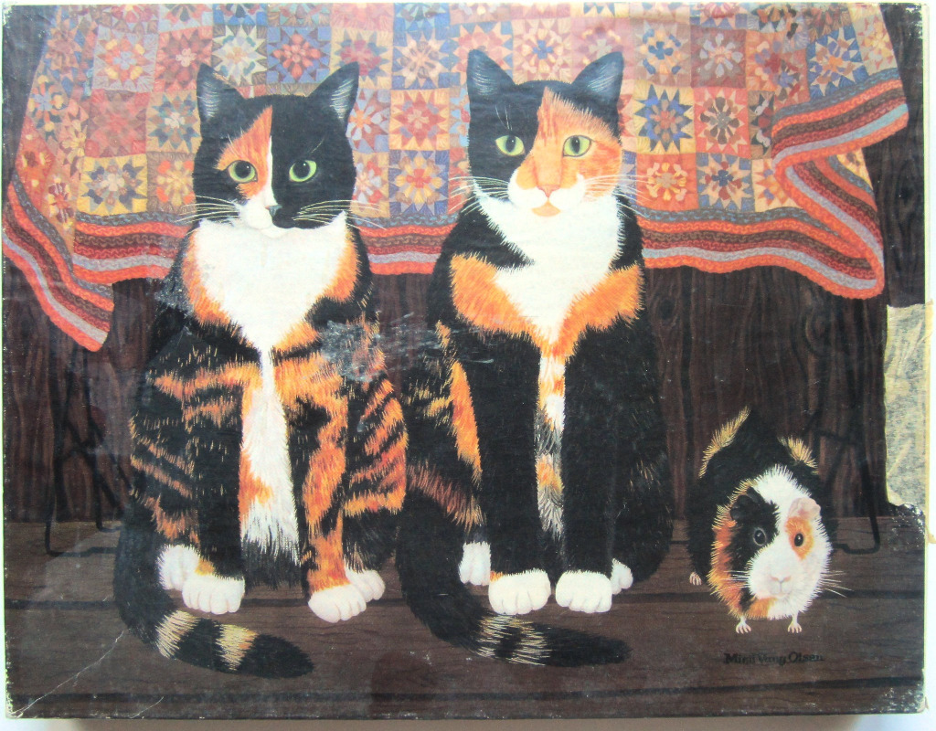 Two calico cats and a guinea pig sitting in front of a patterned quilt