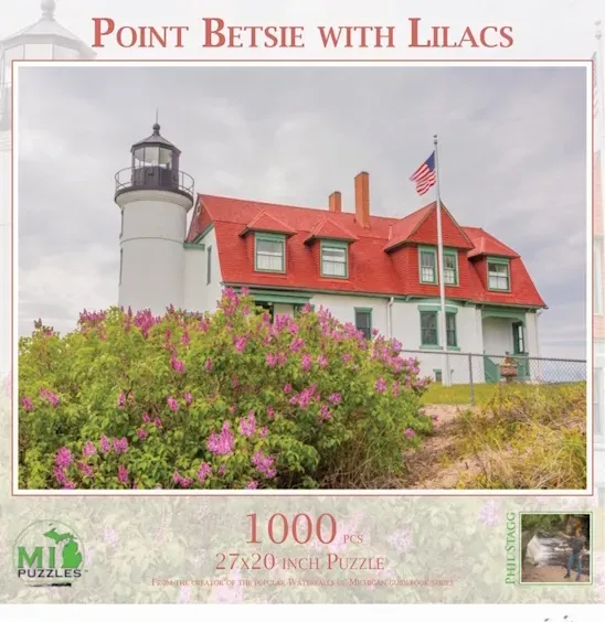A white lighthouse with a bright red roof and green trim, surrounded by a large bush of purple lilacs.