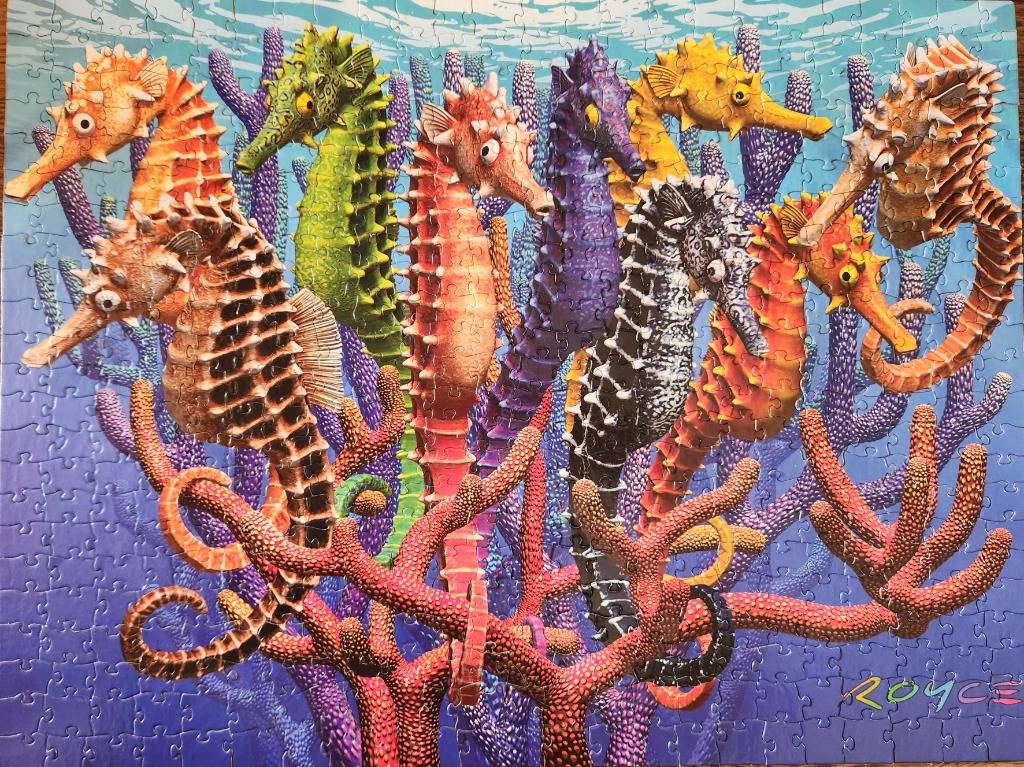 A group of colorful seahorses in various shades standing amidst vibrant coral against a blue underwater background.