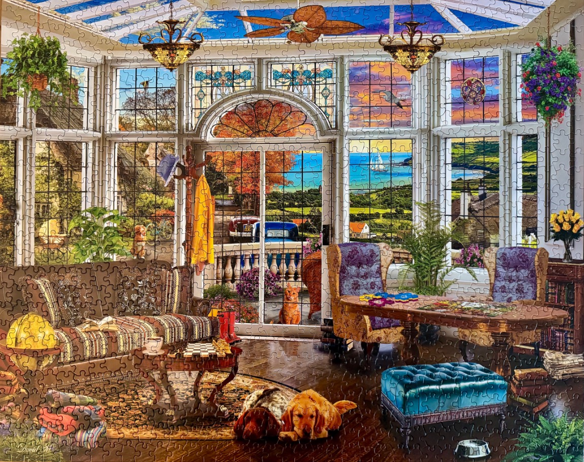 A cozy sunroom interior overlooking a seaside landscape at sunset.