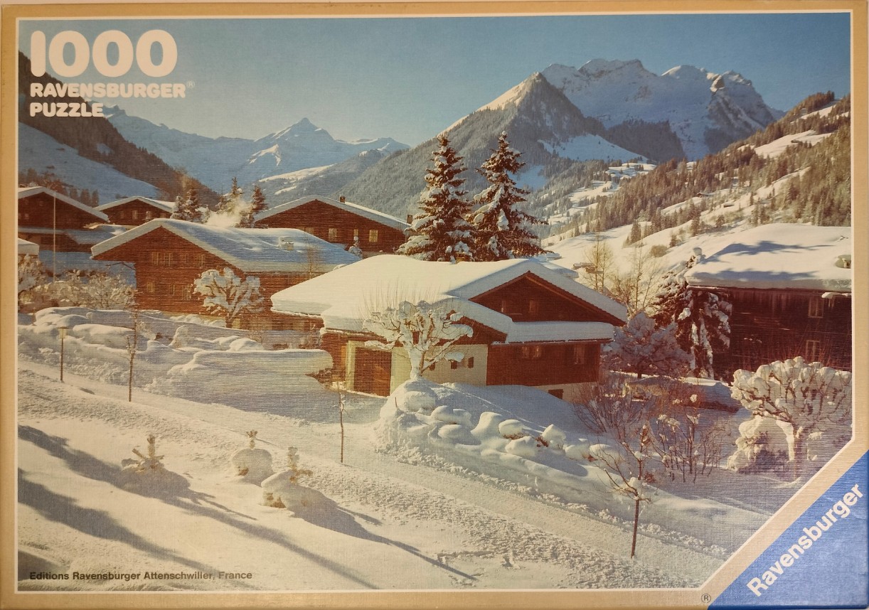 A sunny winter alpine village scene featuring traditional wooden chalets nestled in deep snow with jagged mountains behind.