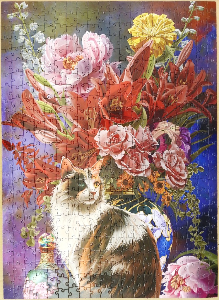 A long-haired calico cat sits in front of a vibrant, ornate floral arrangement with a deep blue and purple background.