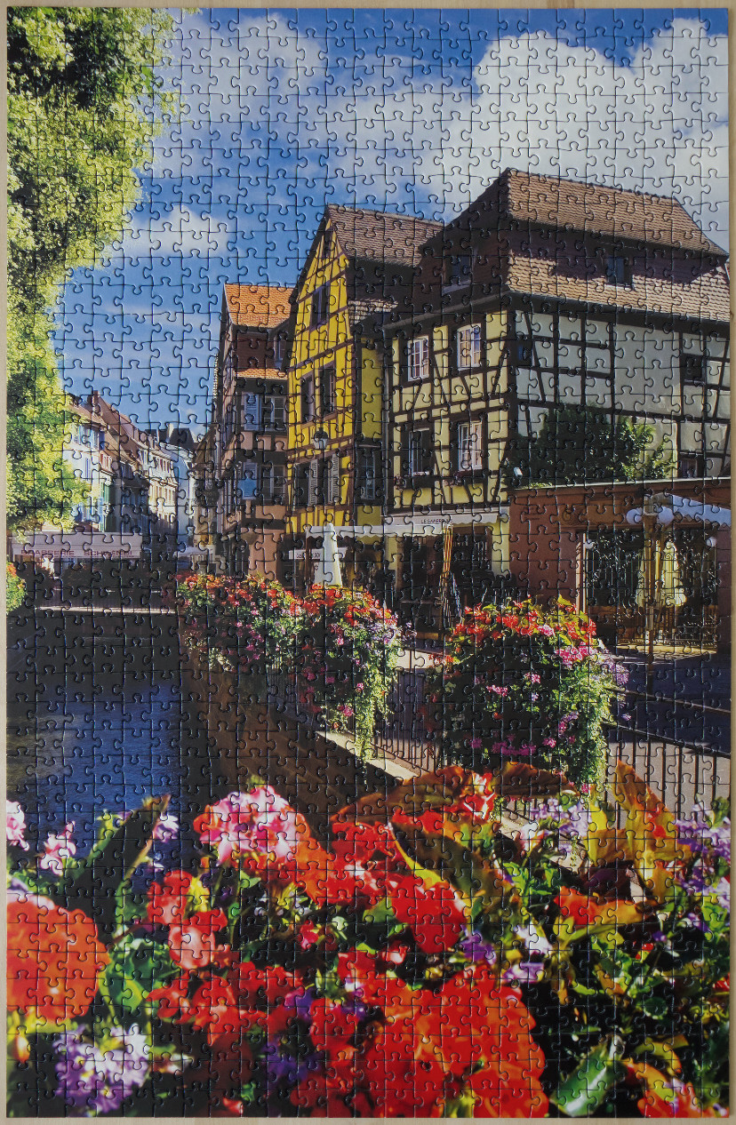 A scenic view of half-timbered houses along a canal filled with vibrant flowers in Colmar, France.