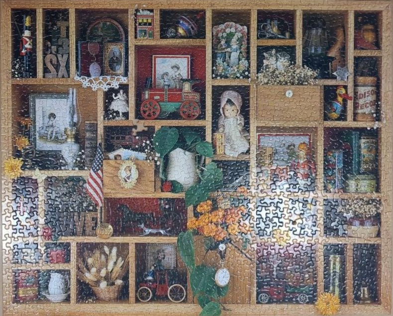 A wooden printer's tray filled with a collection of antique toys, photographs, and floral decorations.