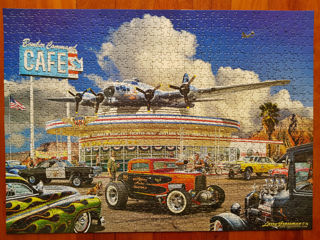Retro 1950s-style diner with a vintage bomber plane on the roof surrounded by classic hot rods.