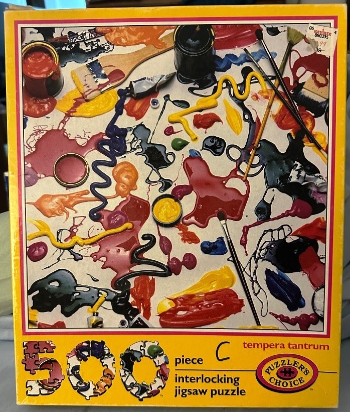 Artistic arrangement of spilled colorful tempera paint, paintbrushes, and open paint tins on a white surface.