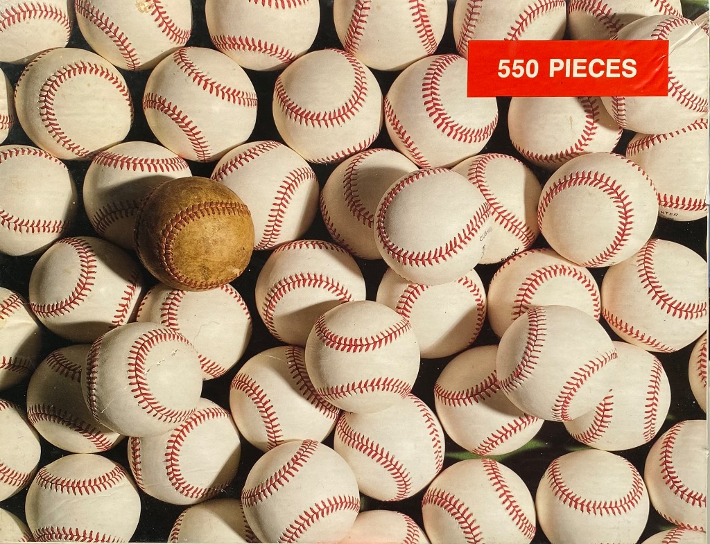 A close-up, top-down view of many white baseballs with red stitching, with one single weathered brown baseball.