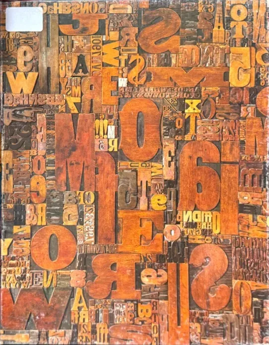 A close-up view of vintage wooden letterpress blocks arranged in a dense, chaotic collage.