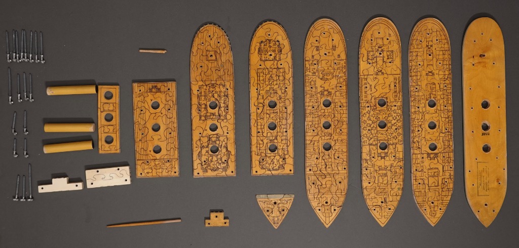 A top-down view of wooden model ship deck sections and metal hardware arranged on a gray surface.