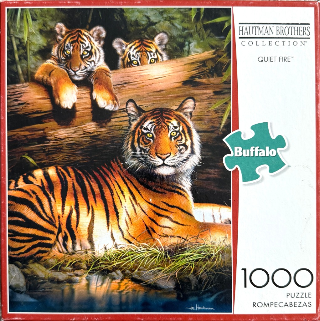 An illustration of an adult tiger lounging in tall grass by a stream with two tiger cubs peeking over a log behind it.