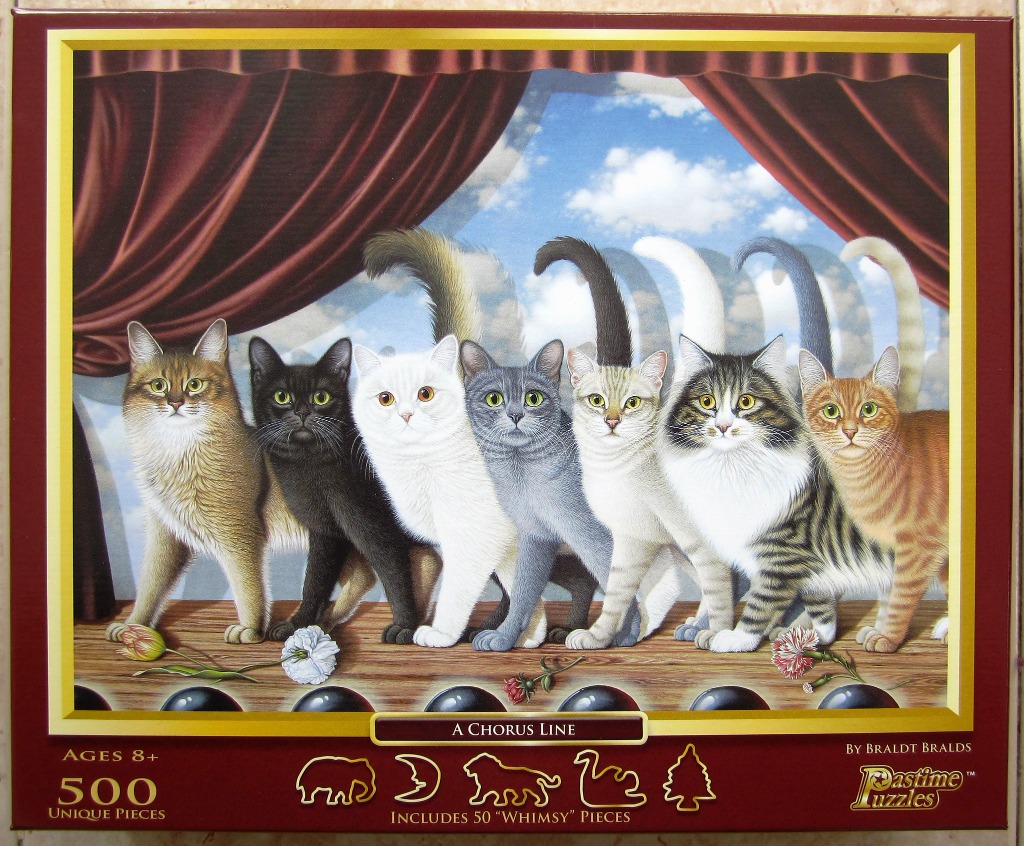 Seven cats of different colors standing in a line on a wooden stage in front of theater curtains.