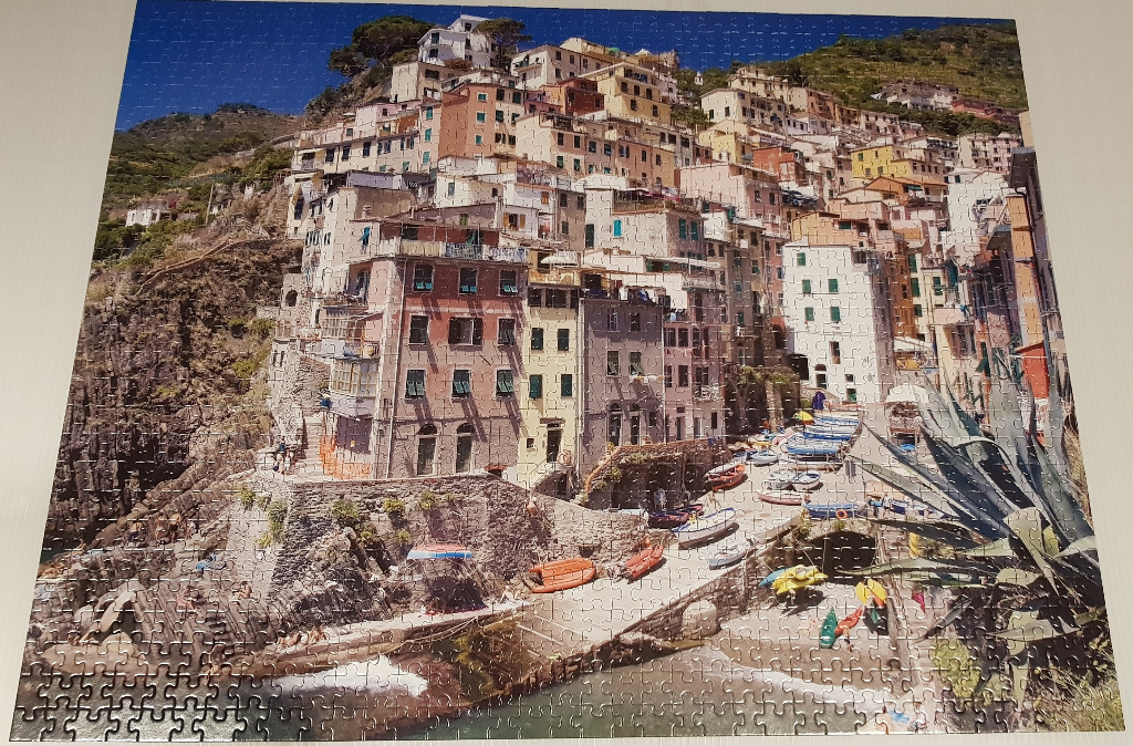 A sunny photograph of the village of Riomaggiore in Italy with colorful buildings stacked on a cliffside.