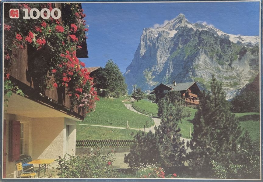 Scenic photograph of a Swiss alpine village with vibrant red geraniums and a looming mountain peak in the background.