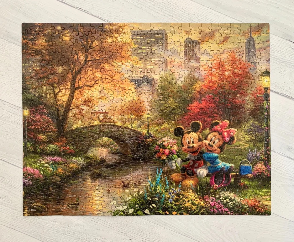 Mickey and Minnie Mouse sitting on a bench in a vibrant, sunlit autumn park with a stone bridge.